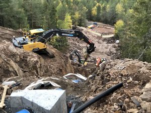 Bilde: Gravemaskin som står i bratt terreng og legger ned nye vannrør.