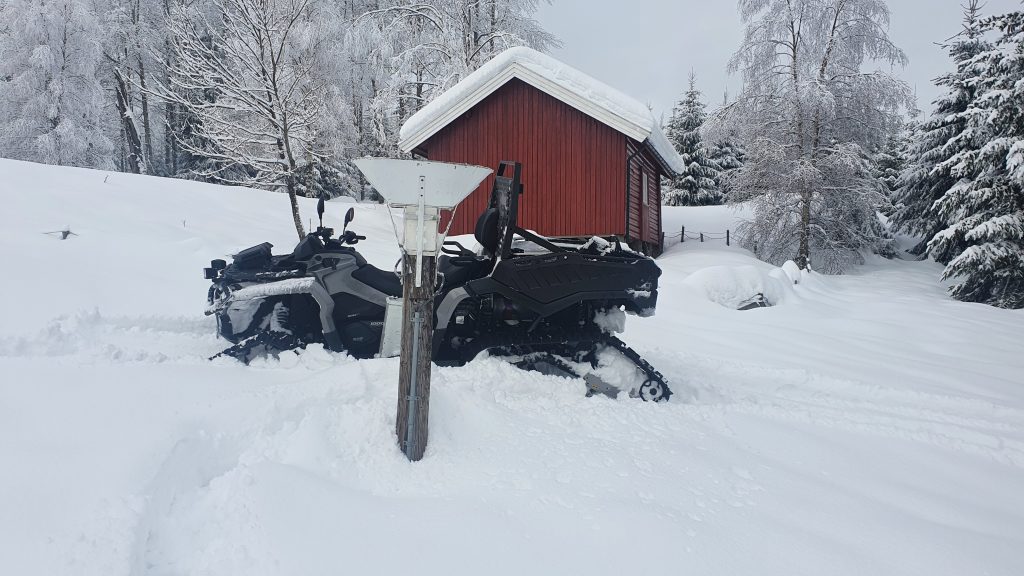 En ATV står i snøen ved en manuell nedbærsmåler. 