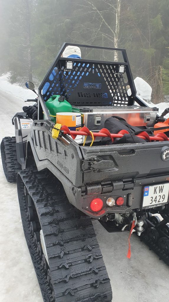 En ATV står på en skogsvei. I hengeren er det et isbor og annet utstyr. 