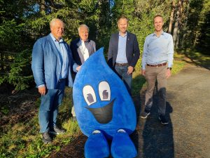 Bilde: tre menn står bak en blå dråpe maskot