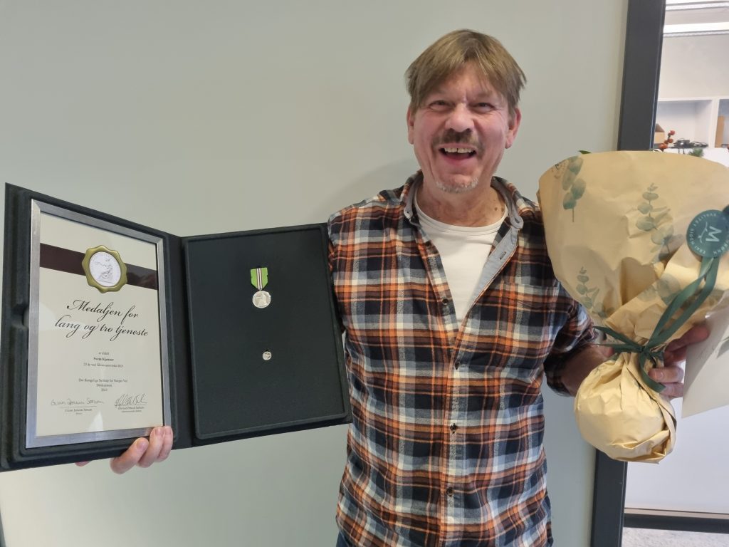Bilde: mann som holder medalje for lang og tro tjeneste og en blomsterbukett